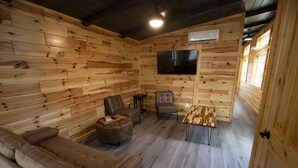 A wooden-paneled room with a sofa, two chairs, a small table, and a TV mounted on the wall. - SUADA-Superior ADA Cabin (Park City)