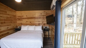 A wooden cabin bedroom with a bed, nightstands, and a window overlooking a deck. - SUADA-Superior ADA Cabin (Park City)