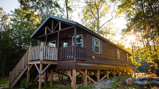 A wooden cabin with a deck and stairs, surrounded by trees.