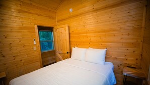 A wooden cabin bedroom with a bed, a small table, and a window.