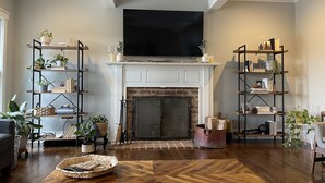 A living room with a fireplace, wooden flooring, and two bookshelves filled with books and plants. - Private Pool, 1st Floor Bedroom, Hershey Park, Ski Roundtop, Yellow Breeches. (Mechanicsburg)
