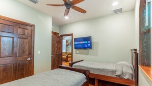 A bedroom with two wooden beds, a ceiling fan, and a TV on the wall.