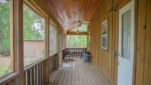 A wooden deck with a ceiling fan, a covered seating area with chairs, and a door on the right.