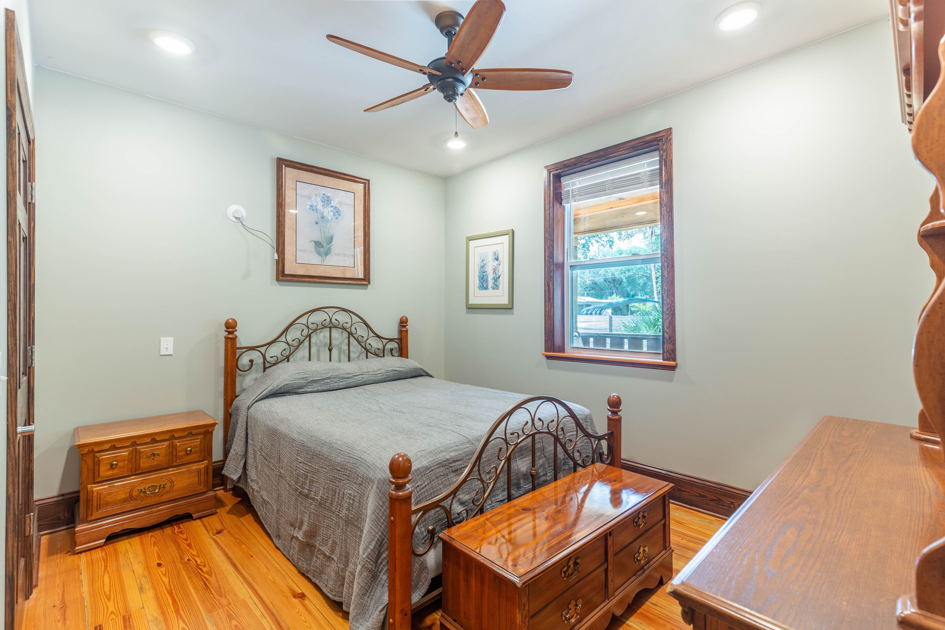 A bedroom with a wooden bed, a nightstand, a dresser, and a window with blinds.