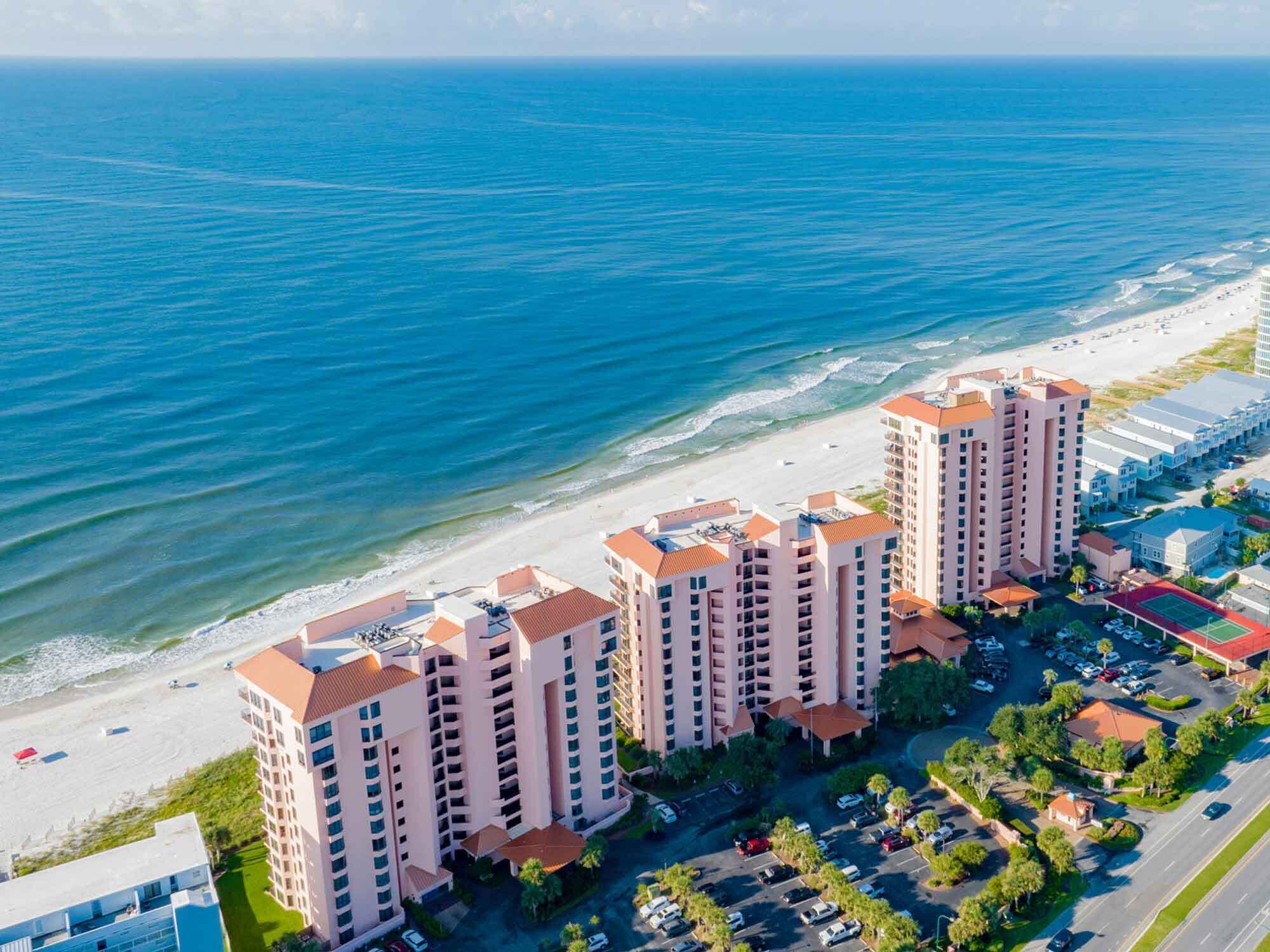 A coastal hotel with multiple high-rise buildings, a beachfront, and a parking area.
