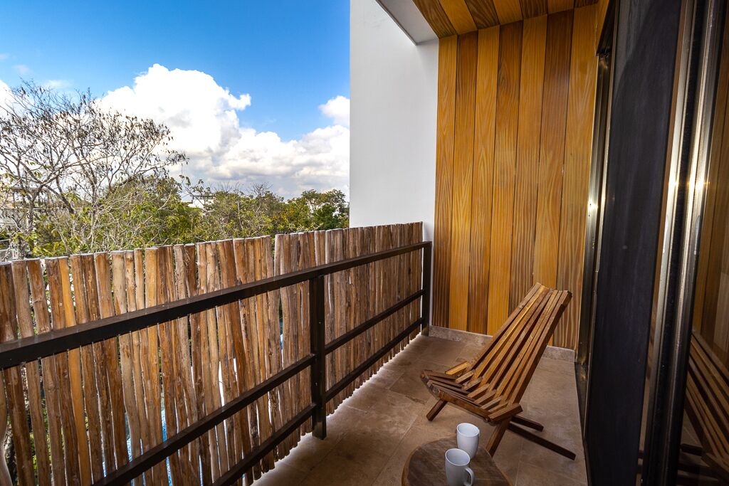 A balcony with a wooden fence, a wooden chair, and a small table with two cups.