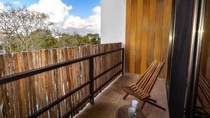 A balcony with a wooden fence, a wooden chair, and a small table with two cups. - Gaia 1-BR Suite (Tulum)