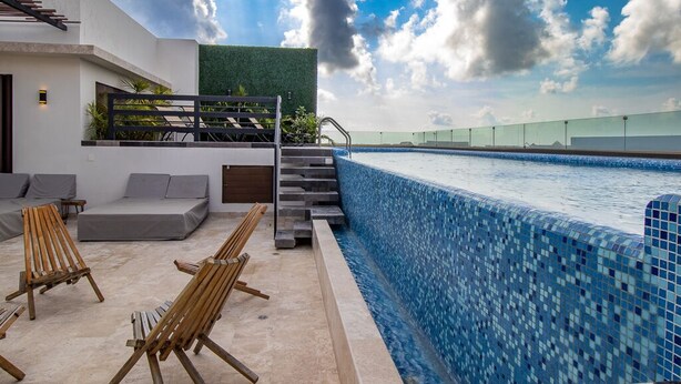 A modern pool area with a mosaic-tiled edge, a staircase leading to a rooftop garden, and wooden lounge chairs. - Gaia 1-BR Suite (Tulum)