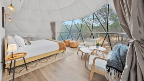 A spacious tented room with a bed, seating area, and large windows offering a view of the outdoors. - Boutique Resort for Weddings & Retreats w/ Pool, Wellness, Pickleball, & More! (Wimberley)