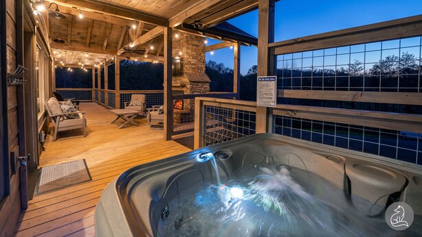 Un bain à remous sur une terrasse en bois, avec une cheminée en pierre, des sièges d’extérieur et une vue sur le ciel nocturne.