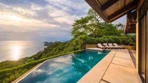 Una piscina infinitàtica amb vistes a l'oceà, envoltada de vegetació exuberant i una estructura d'edifici modern.