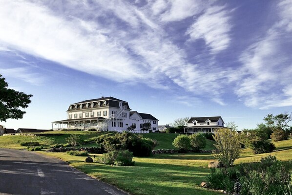 A large white building with a balcony, surrounded by greenery and a clear sky.