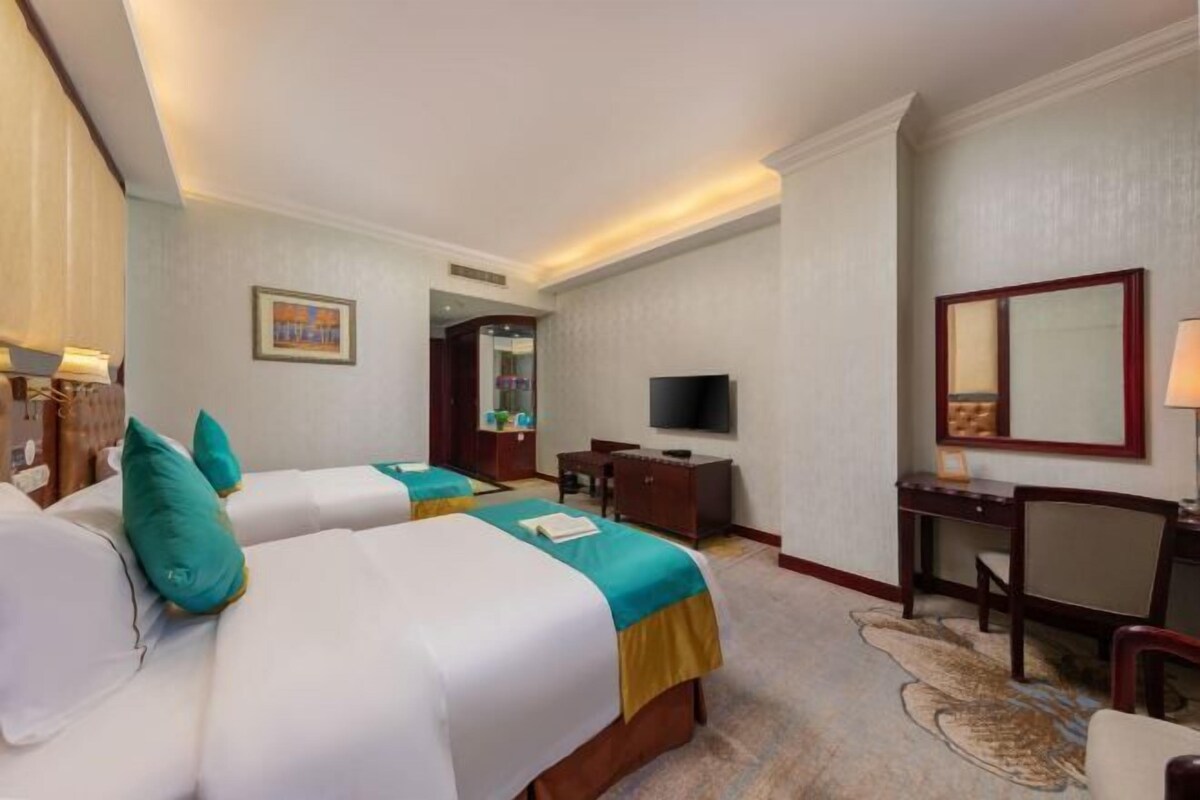 Una habitación de hotel con dos camas, un escritorio, un televisor y un espejo.