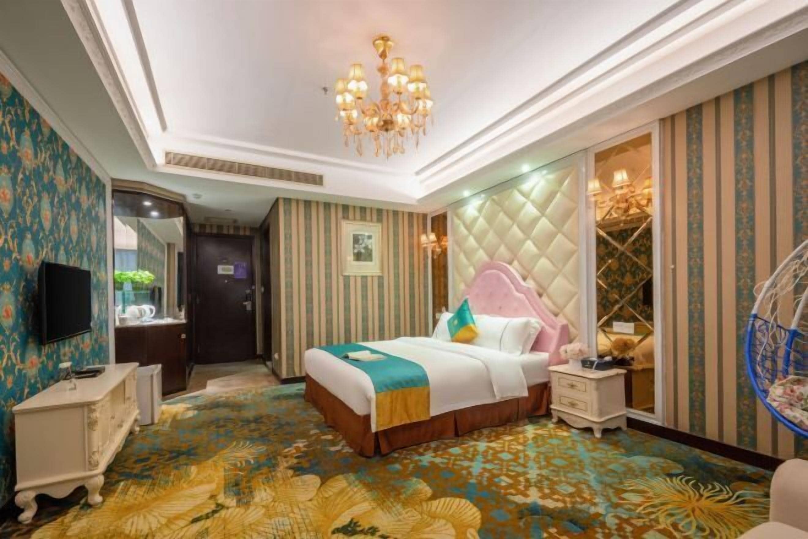 Una habitación de hotel con cama, mesitas de noche, televisor, candelabro y alfombra estampada.