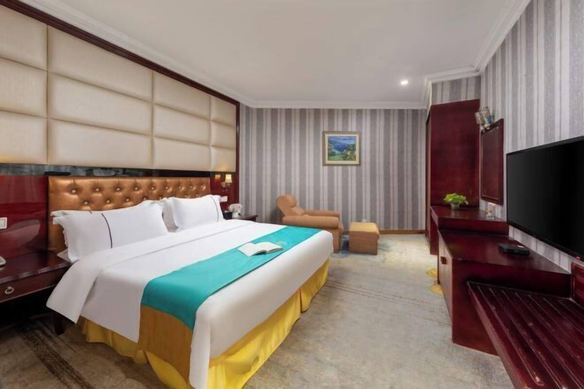 A hotel room with a large bed, a television, a seating area, and a painting on the wall.