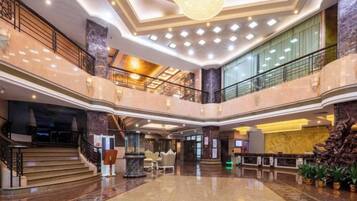 A multi-level hotel lobby with a grand staircase, a reception desk, and a chandelier.
