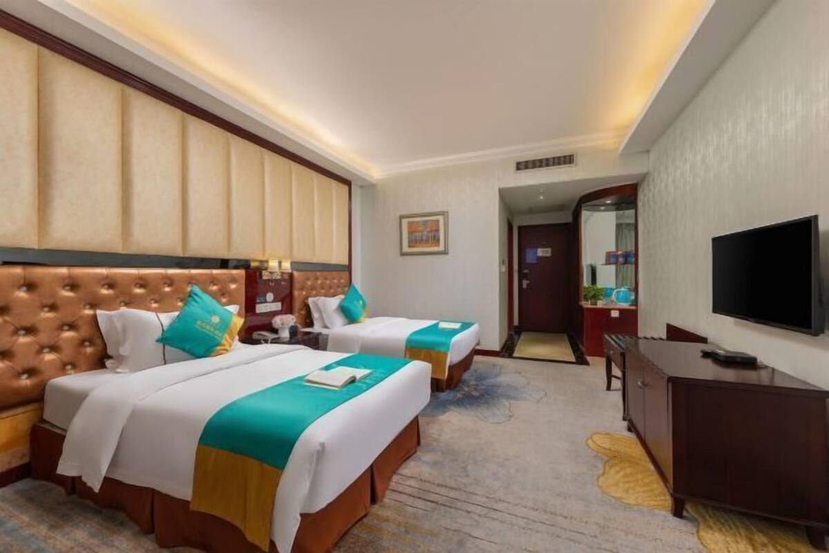 A hotel room with two beds, a TV, a desk, and a mirror.