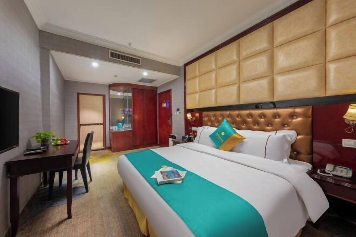 A hotel room with a large bed, a desk, a chair, and a television.