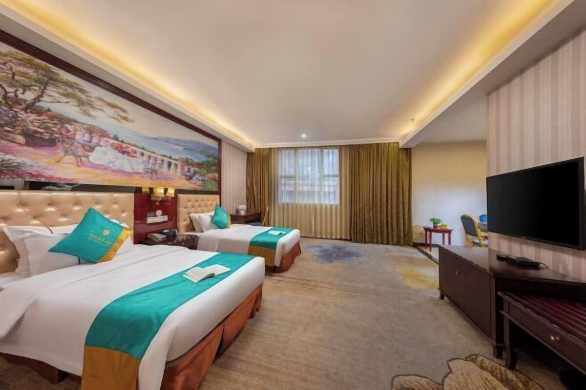 A hotel room with two beds, a television, a painting on the wall, and a window with curtains.