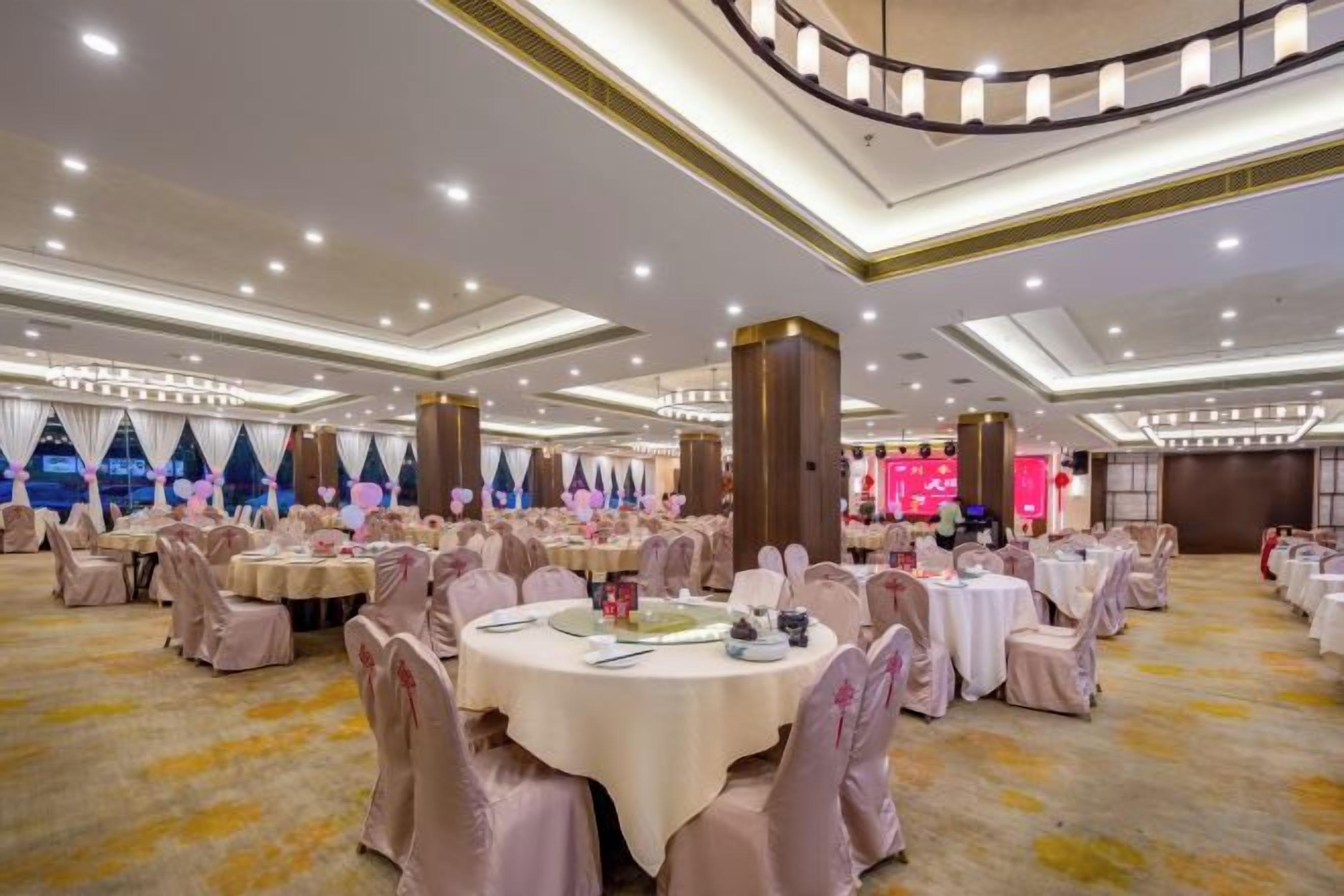 A banquet hall with round tables, chairs, and a stage.
