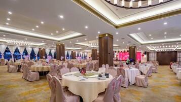 A banquet hall with round tables, chairs, and a stage.
