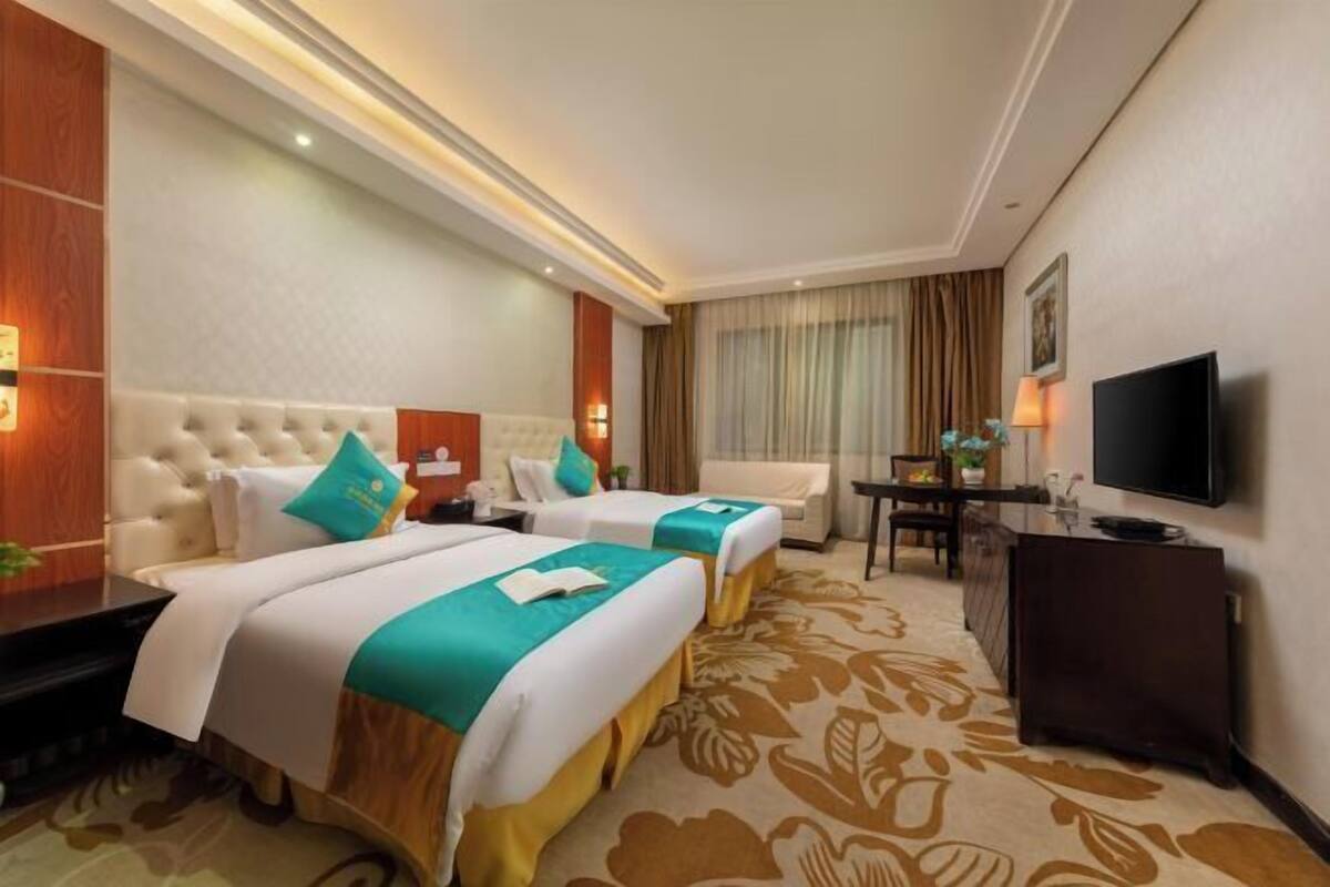 A hotel room with two beds, a TV, a desk, and a large window.