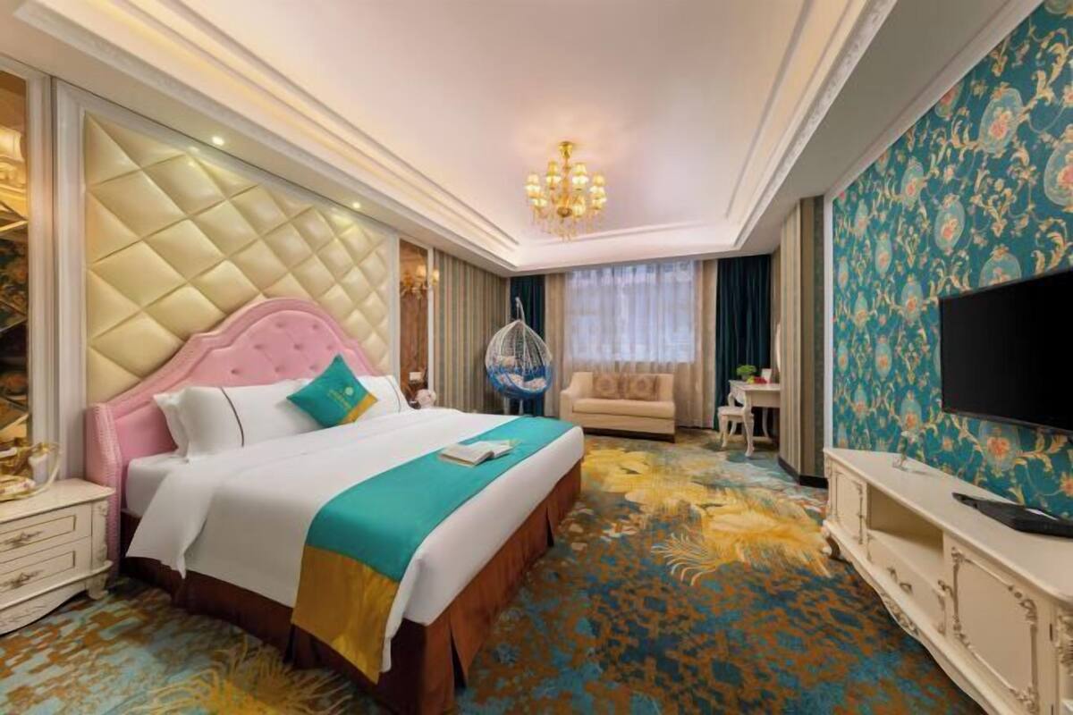 A hotel room with a large bed, a television, a chandelier, and a patterned carpet.