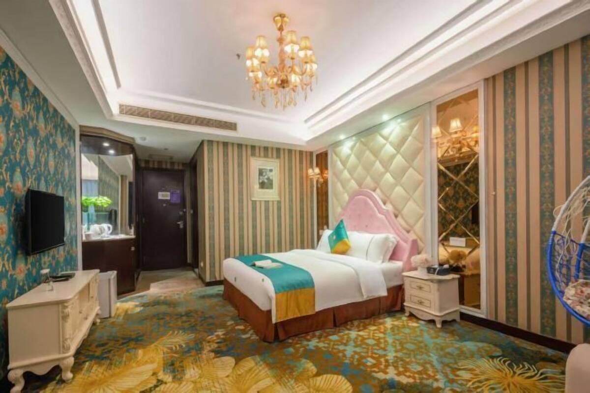 A hotel room with a large bed, a television, a bedside table, a wardrobe, and a chandelier.