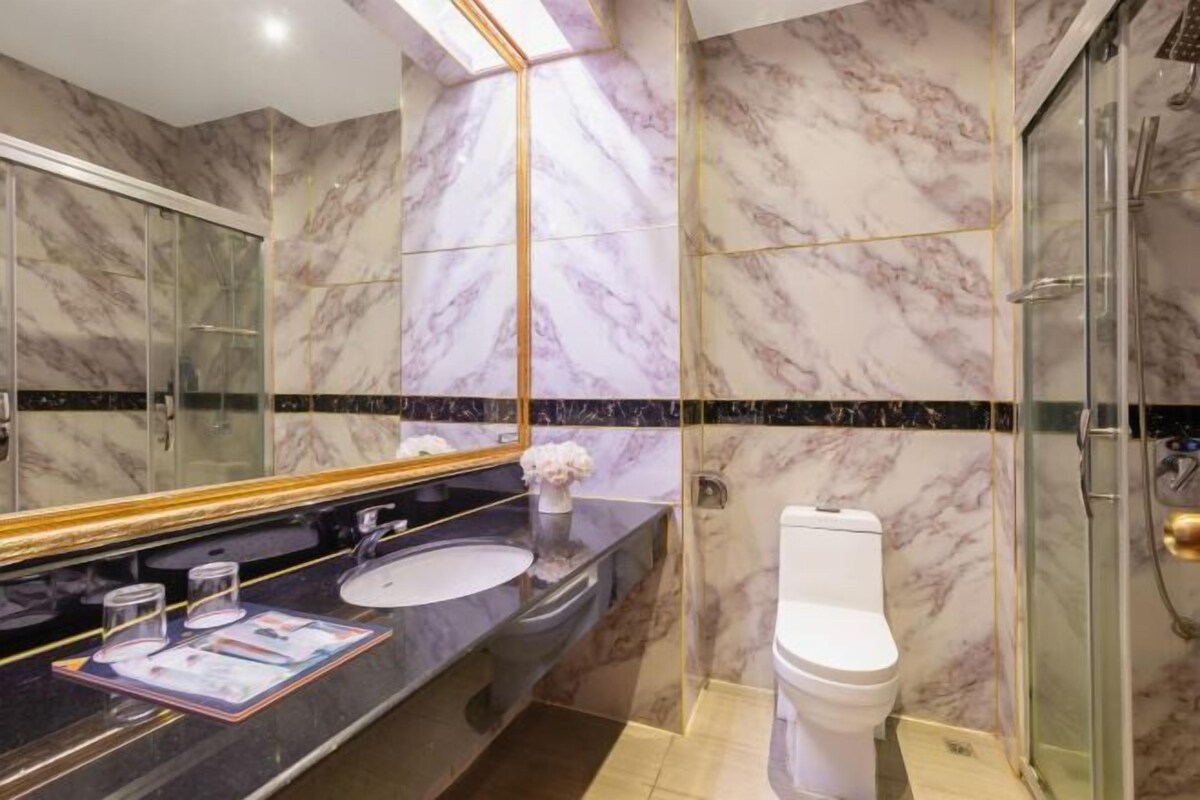 Un baño moderno con paredes de mármol, cabina de ducha de vidrio y encimera negra con lavabo y espejo.
