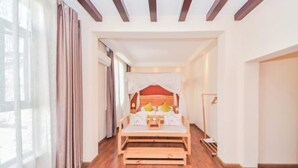 Een kamer met een houten bed, een nachtkastje en een bijzettafeltje. Links is een raam met gordijnen.