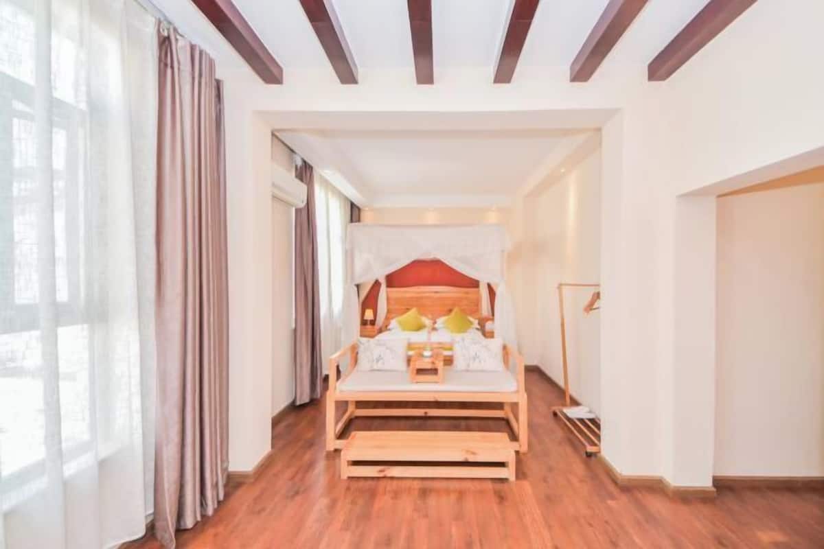 A room with a wooden bed, a bedside table, and a nightstand. There is a window with curtains on the left side.