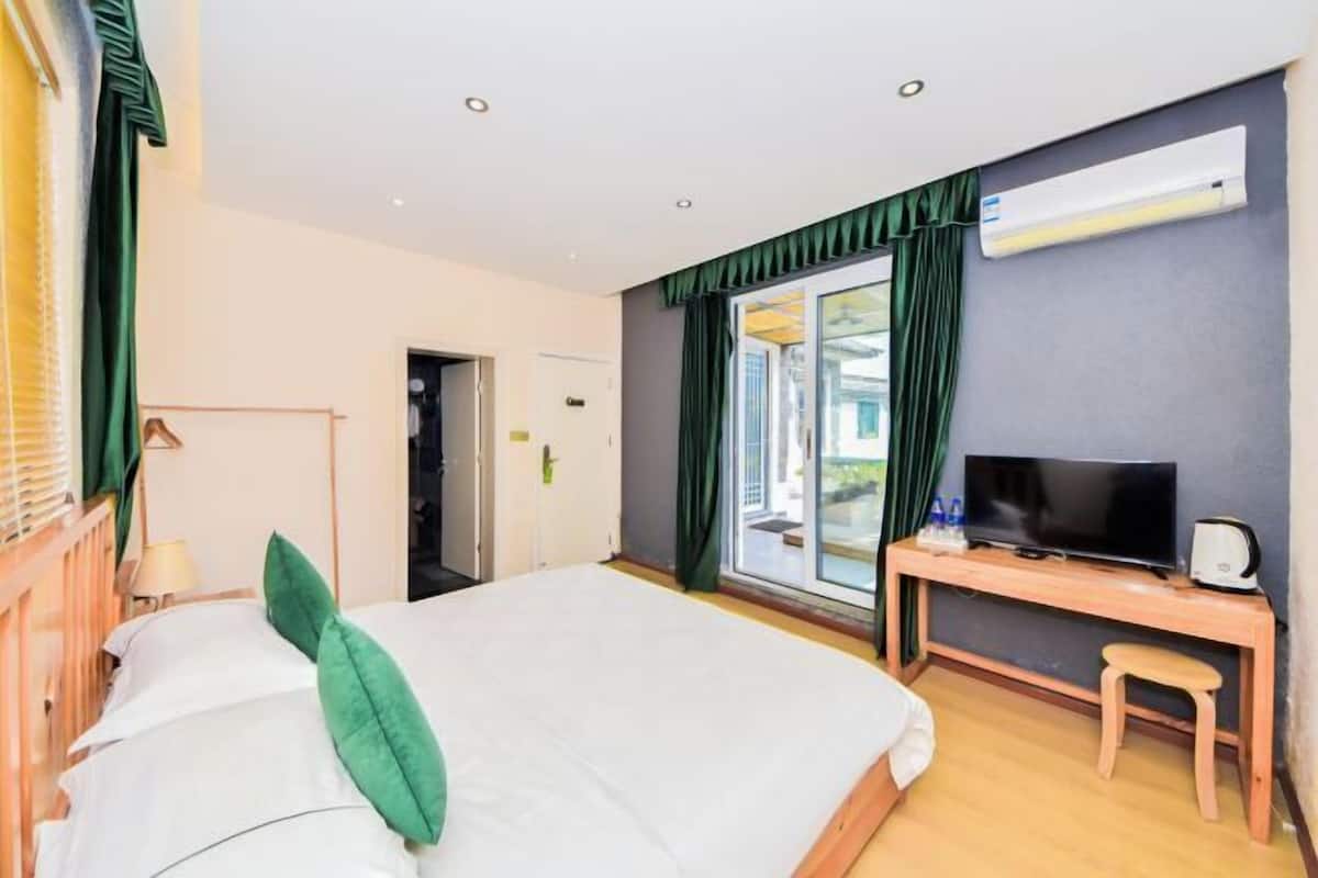A hotel room with a bed, a desk with a television, and an air conditioning unit.
