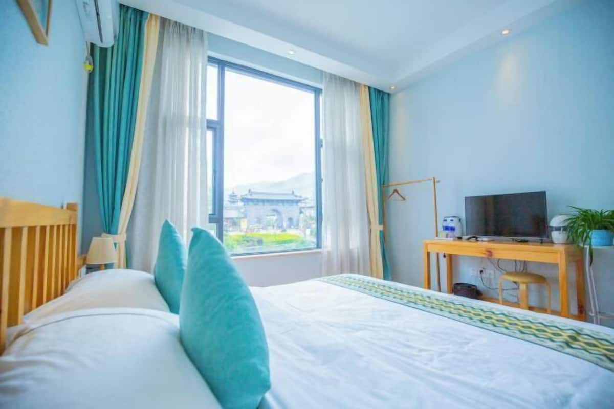 A hotel room with a bed, a TV, a desk, and a window with a view of a building.