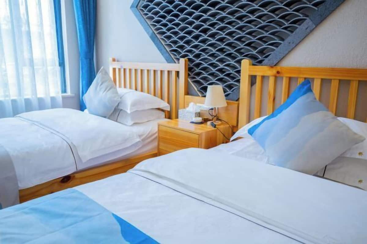 A hotel room with two beds, a nightstand, a lamp, and a unique acoustic panel on the wall.