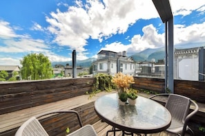 A wooden deck with a round table and chairs, overlooking a mountainous landscape.