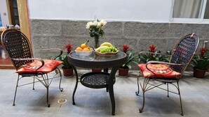 Een ronde tafel met een glazen blad, omringd door rieten stoelen met rode kussens. Op tafel staan potplanten en een schaal fruit.