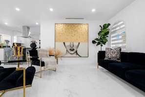 Una sala de estar moderna con un sofá negro, un sillón con marco dorado y un cuadro abstracto grande en la pared.
