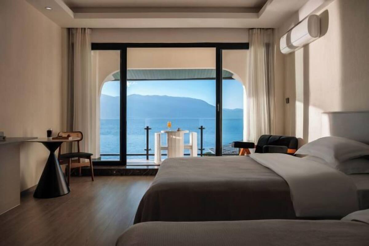 Ein Hotelzimmer mit großem Fenster, einem Bett, einem Schreibtisch und einem Stuhl.