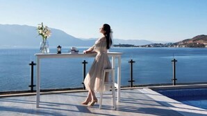 A woman seated at a table with a view of a body of water and mountains in the background. - Golden Silver Bay Seaview Hotel (Dali Shuanglang Branch) (Dali City)
