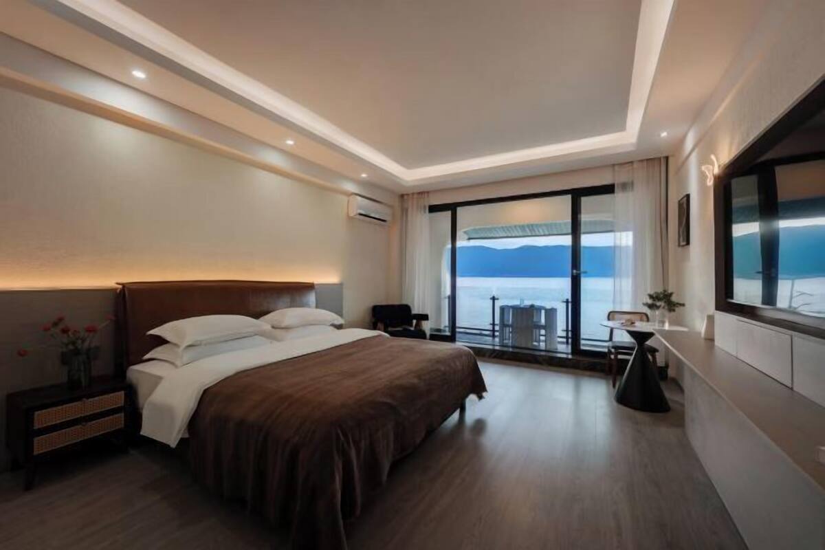 Ein modernes Hotelzimmer mit einem großen Bett, einem Fernseher, einem Essbereich und einem Balkon mit Blick.