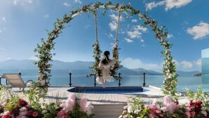 A person on a swing with a floral arch, overlooking a pool and a scenic view. - Golden Silver Bay Seaview Hotel (Dali Shuanglang Branch) (Dali City)