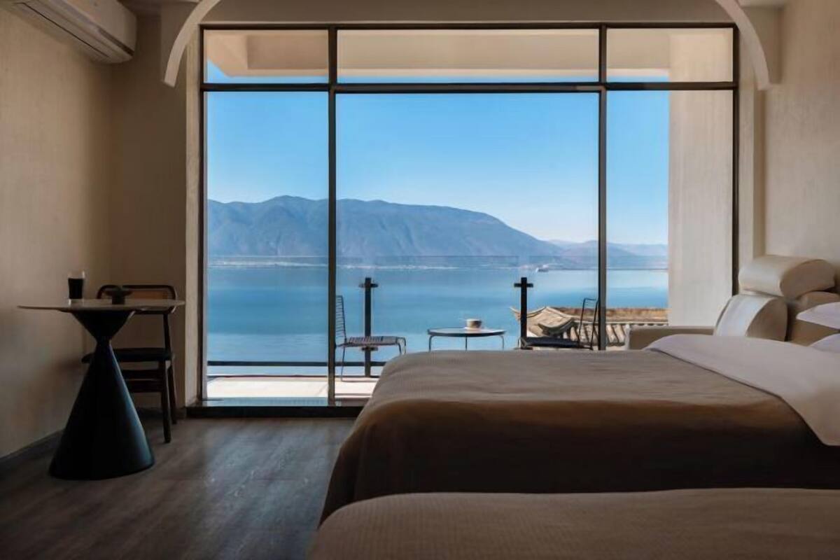 Ein Hotelzimmer mit großem Fenster, einem Bett, einem kleinen Tisch und einem Sessel.