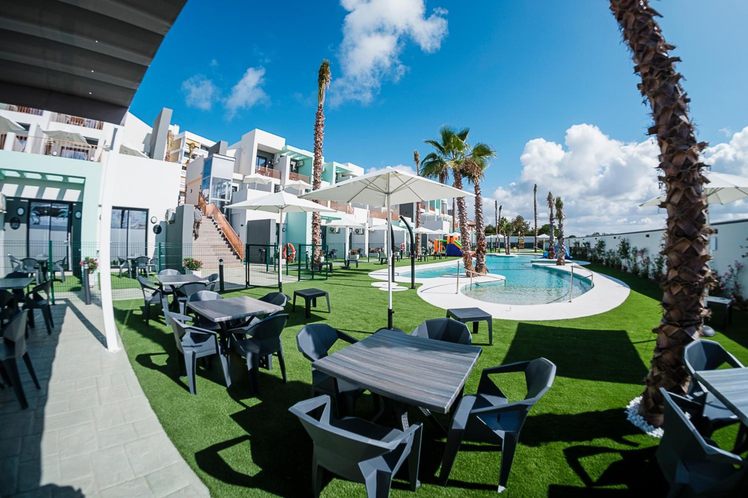 Zona de piscina con césped artificial, mobiliario exterior y cielo despejado.