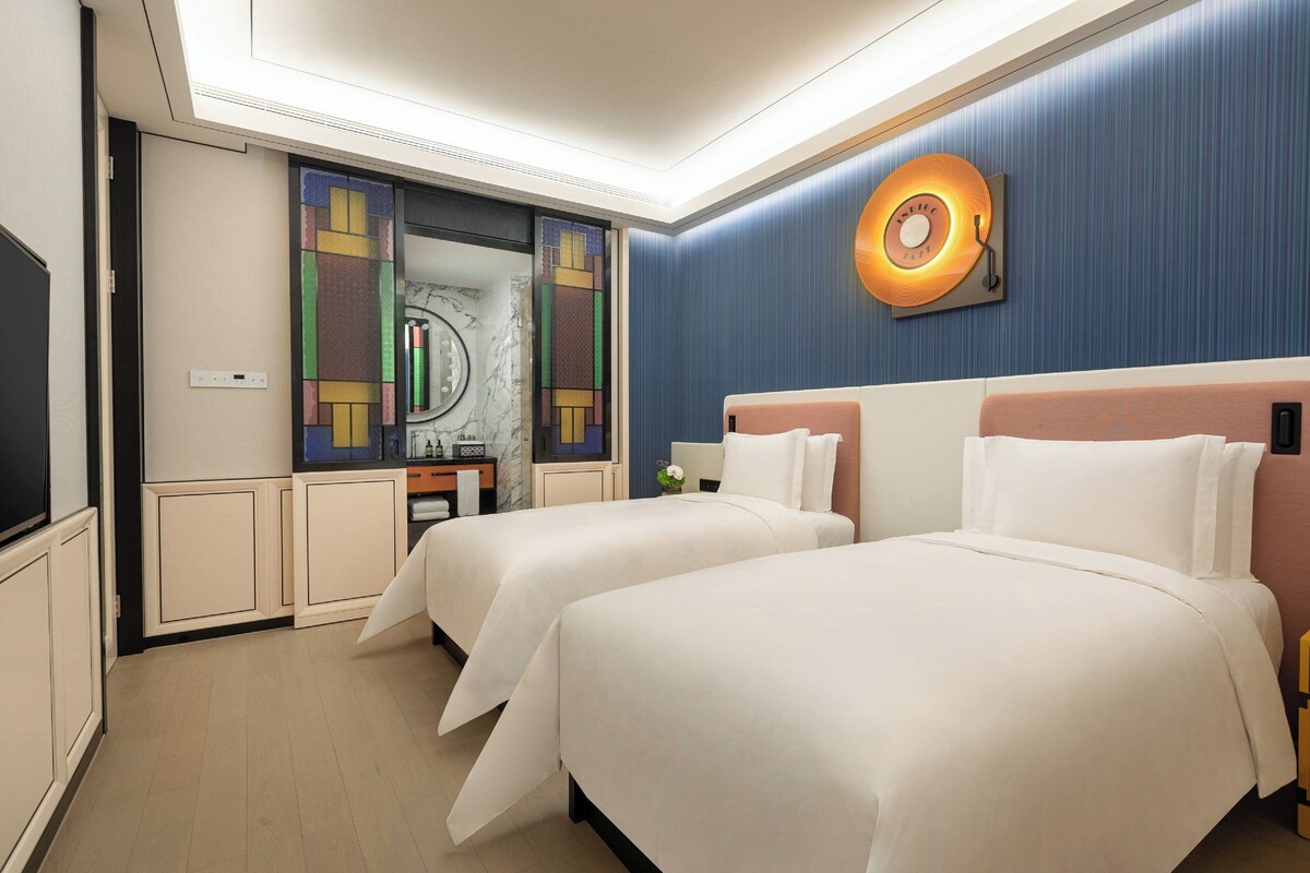 Ein Hotelzimmer mit zwei Betten, einem großen Spiegel, einer Wanduhr und einem kleinen Tisch mit einer Vase.