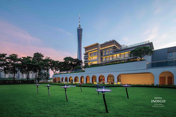 A modern hotel with a rooftop terrace, a tower in the background, and a well-maintained lawn with tables. - Hotel Indigo Guangzhou Haixinsha by IHG (Guangzhou)