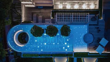 Vista aérea de un hotel con piscina, tres arbustos esféricos y una fuente circular.