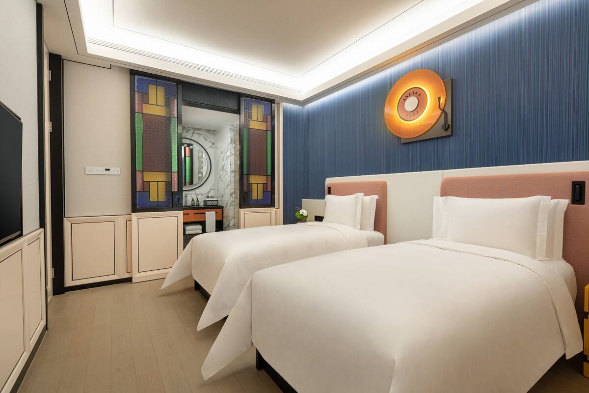 Habitación de hotel con dos camas, un espejo grande, un reloj de pared y una mesita con un jarrón.