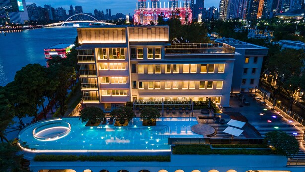 Un hôtel moderne doté d’une grande piscine, de nombreux balcons et offrant une vue sur les toits de la ville au crépuscule.