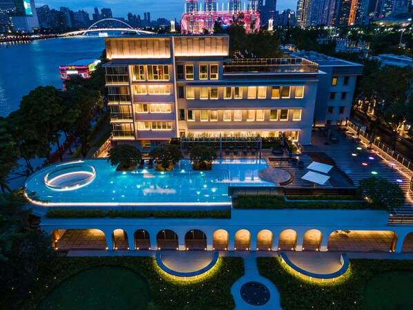 A modern hotel with a large swimming pool, multiple balconies, and a view of the city skyline at dusk. - Hotel Indigo Guangzhou Haixinsha by IHG (Guangzhou)