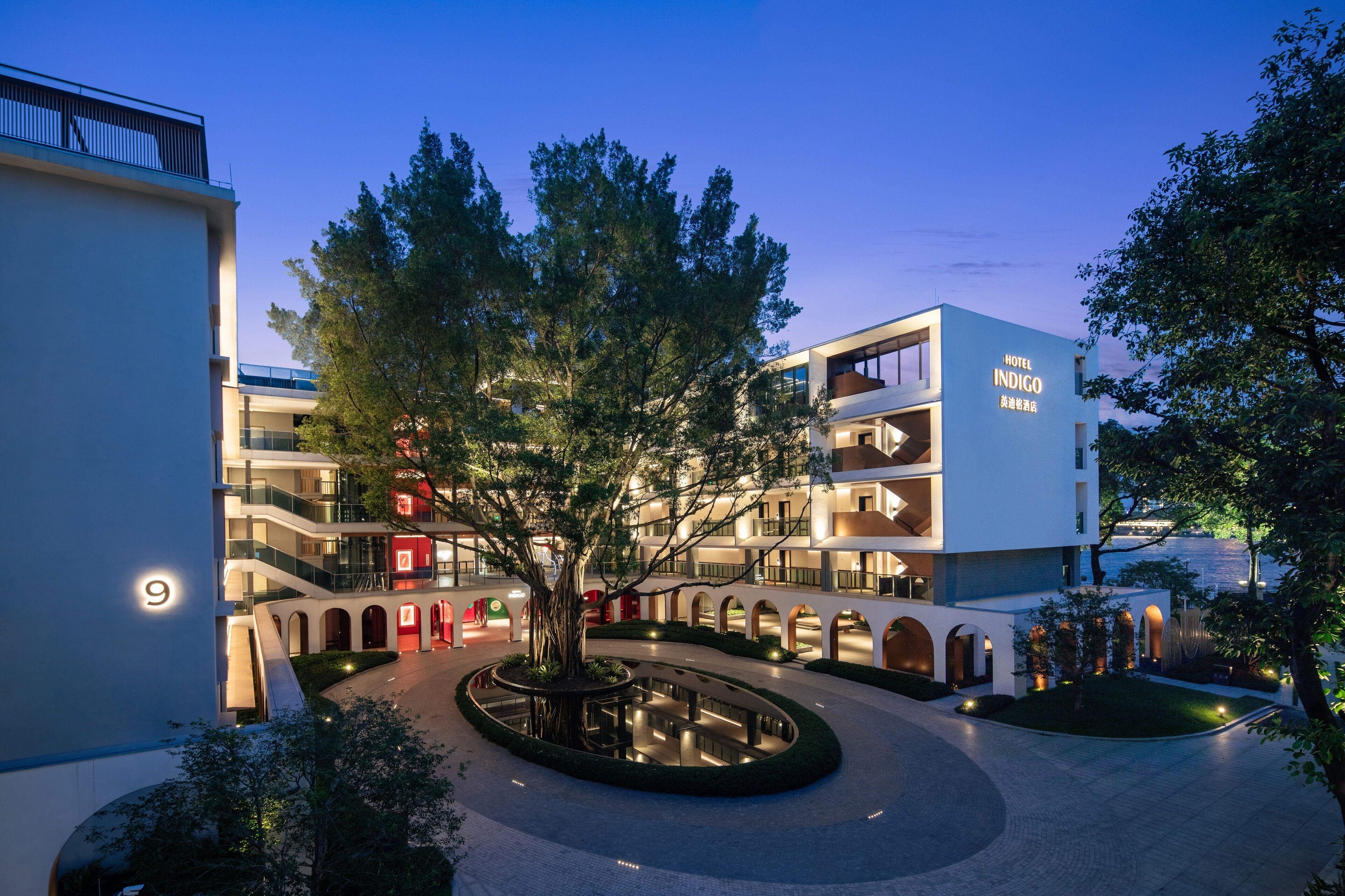 A modern hotel with multiple floors, a central courtyard with a tree, and a visible entrance.